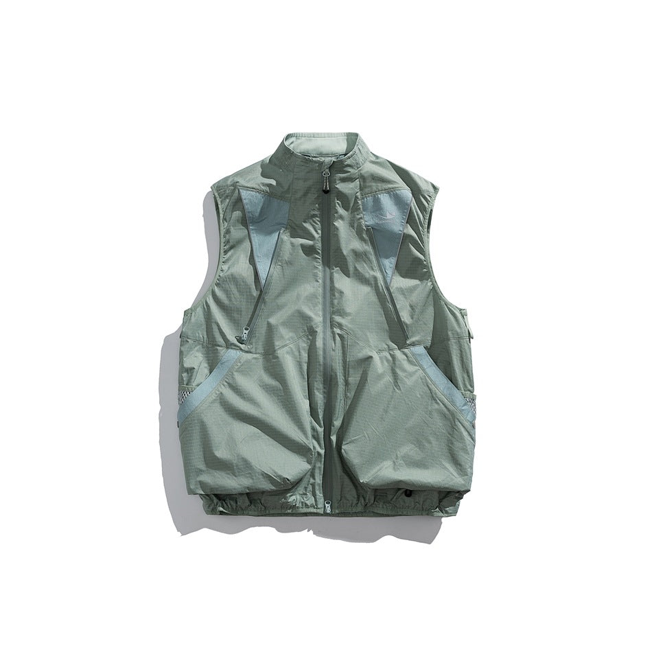 Front view of a sage green sleeveless utility vest with a full zipper, large pockets, and pale blue-gray panels.