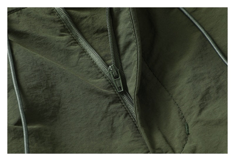 Close-up of a zipper and stitching on dark olive shorts, with a drawcord visible at the edge.