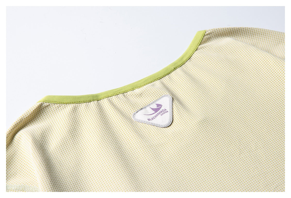Close-up of a green-trimmed neckline and a sewn triangular brand patch on cream dotted fabric.