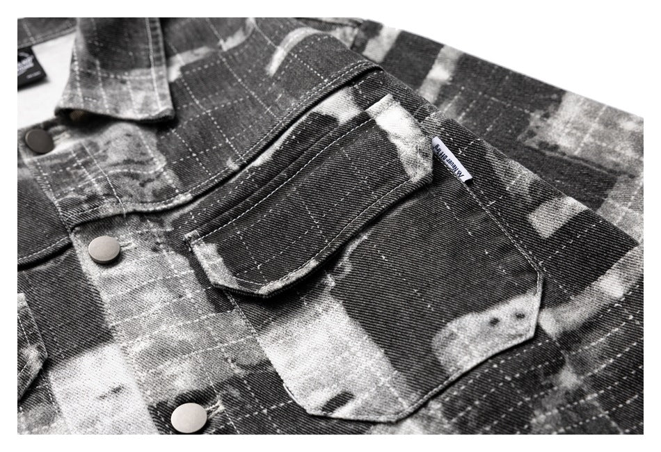 Close-up of a flap chest pocket, woven tab, and snap buttons on the charcoal and gray patterned jacket.