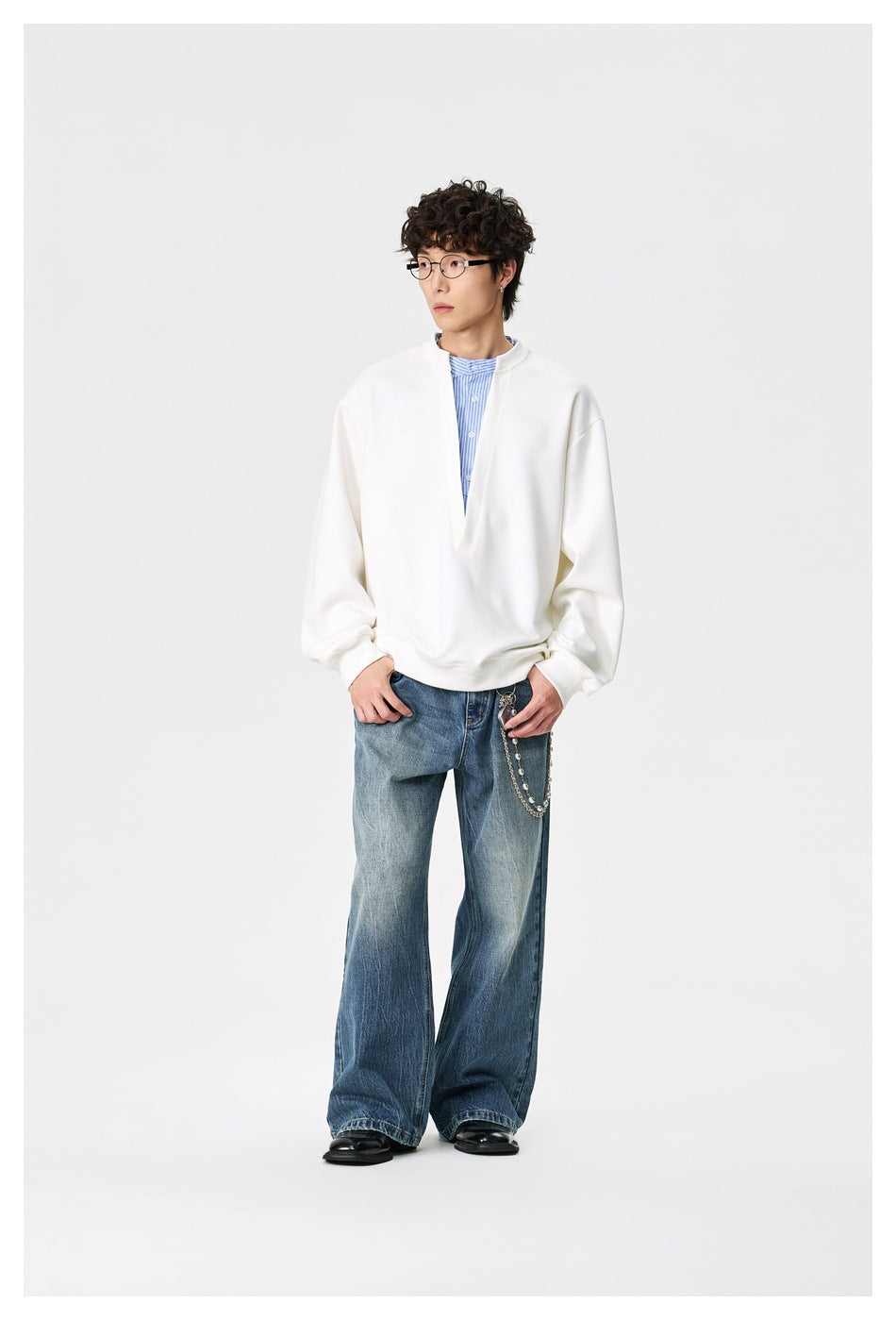 Model wears an oversized white pullover with a deep V neckline over a blue striped shirt and wide-leg blue jeans.