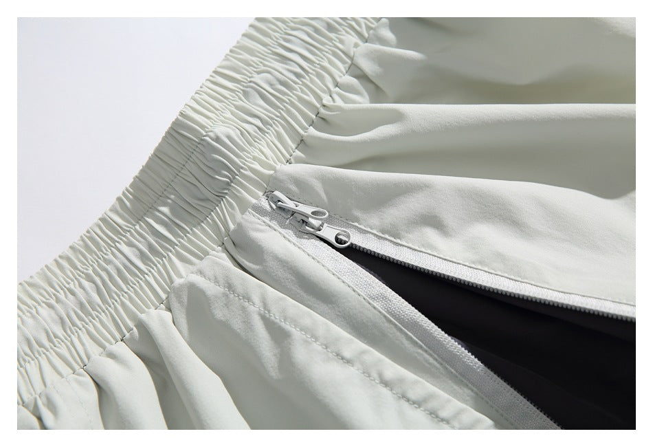 Close-up of pale gray pants with a gathered elastic waistband and partially open zippered pocket.