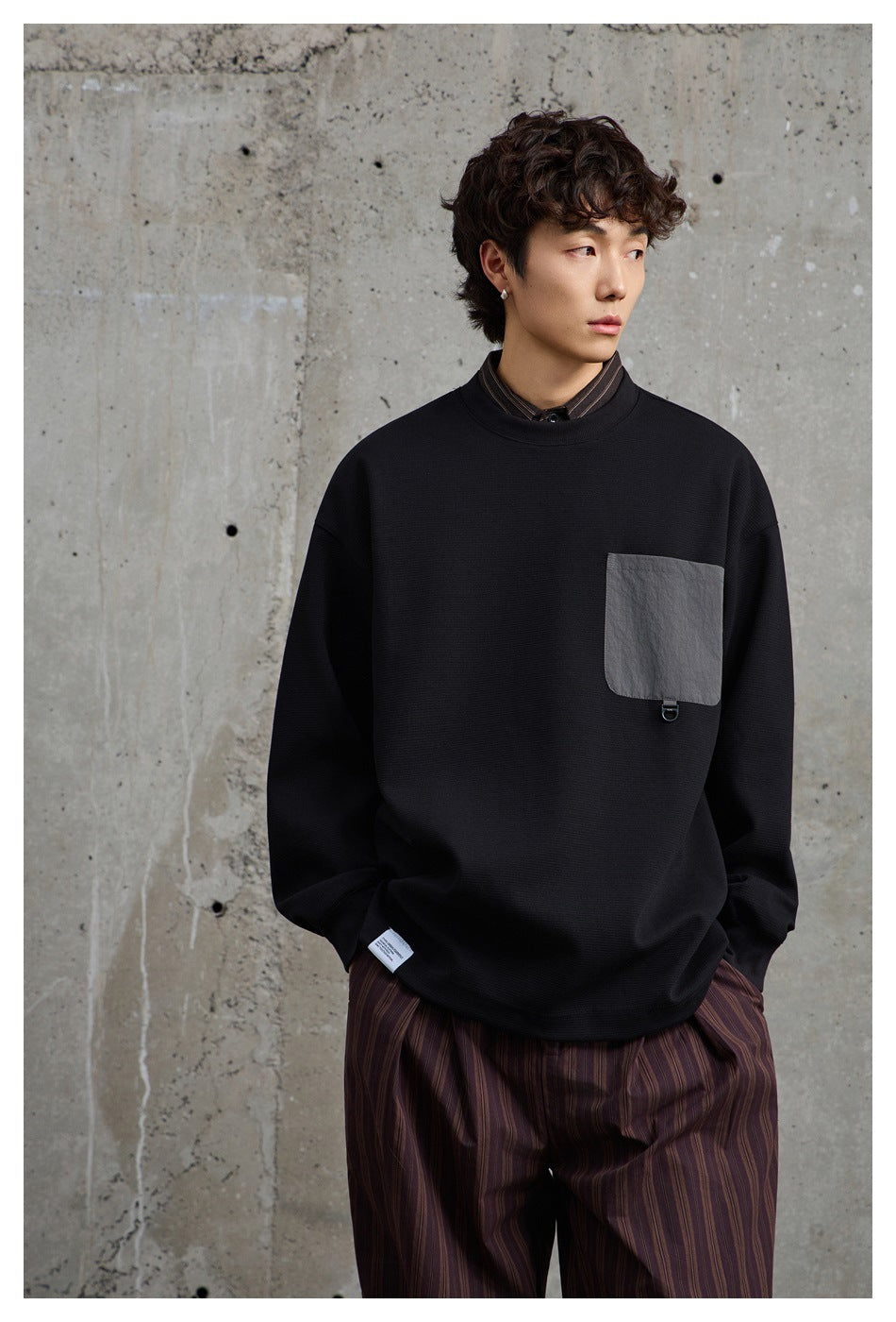 Closer view of a model wearing a black oversized sweatshirt with a gray chest pocket and striped trousers.