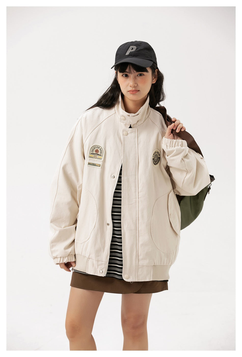 Model wears an ivory oversized jacket with a high collar, front patches, large pockets, and elastic cuffs.