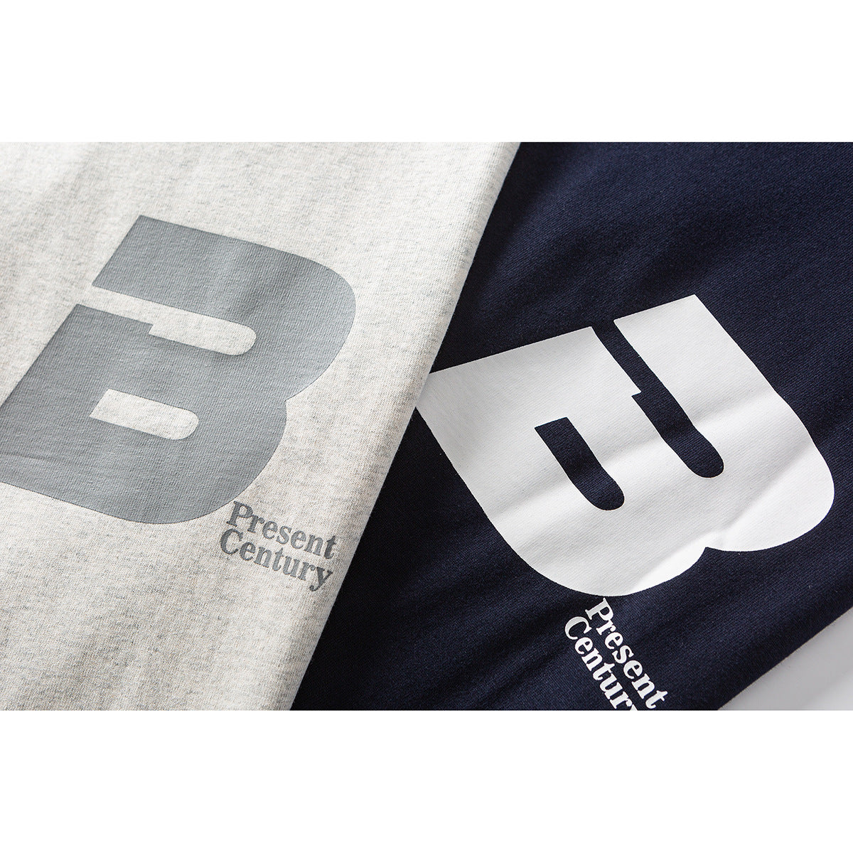 Close-up of heather gray and navy T-shirts showing large contrasting B prints with small “Present Century” text.