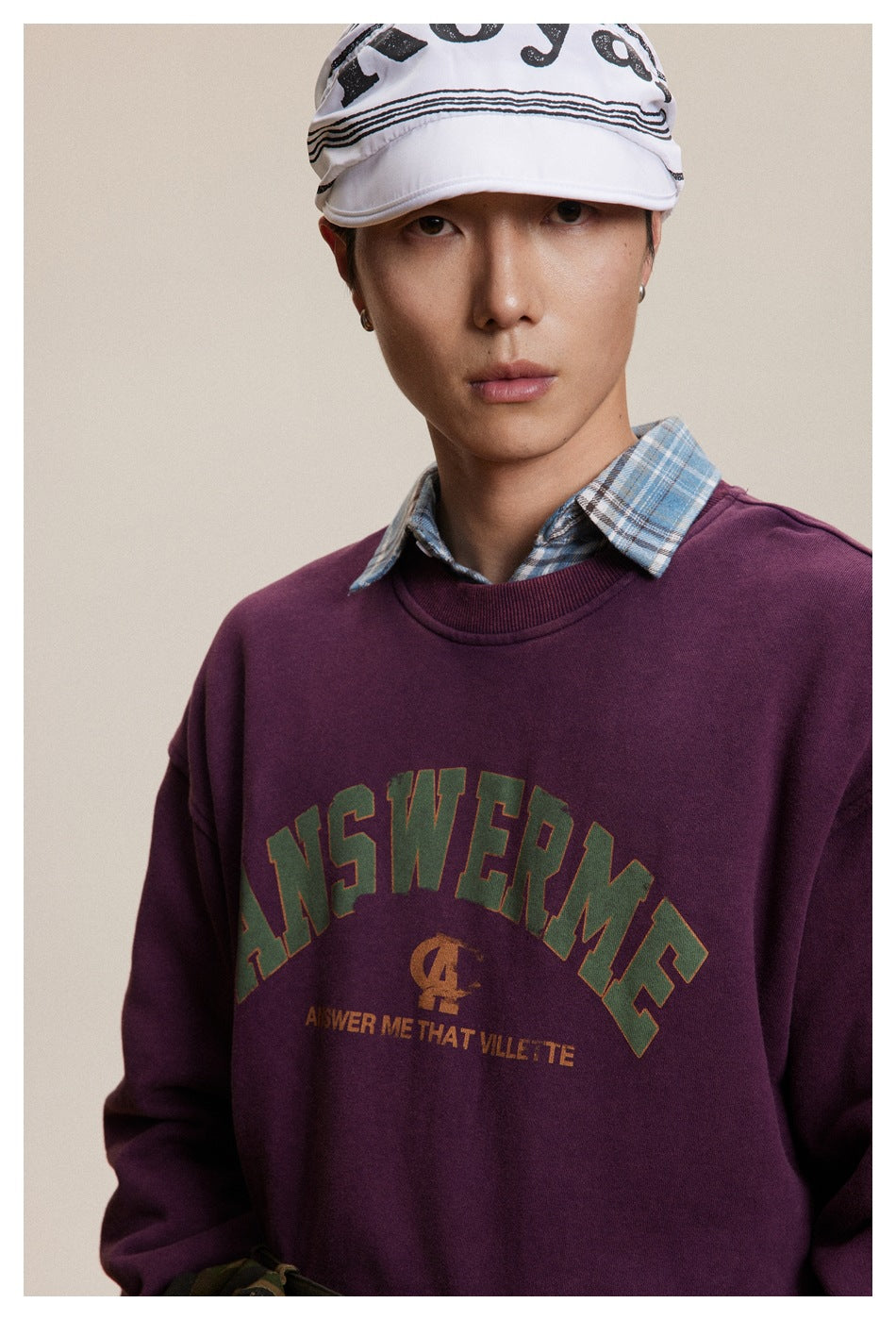 Close-up of a model wearing a burgundy crewneck sweatshirt with arched chest lettering over a blue plaid shirt.