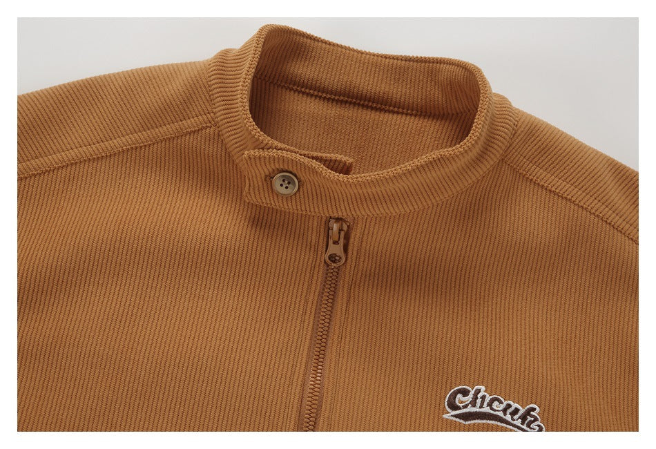 Close-up of a tan ribbed jacket collar, button tab, zipper, and embroidered chest logo.