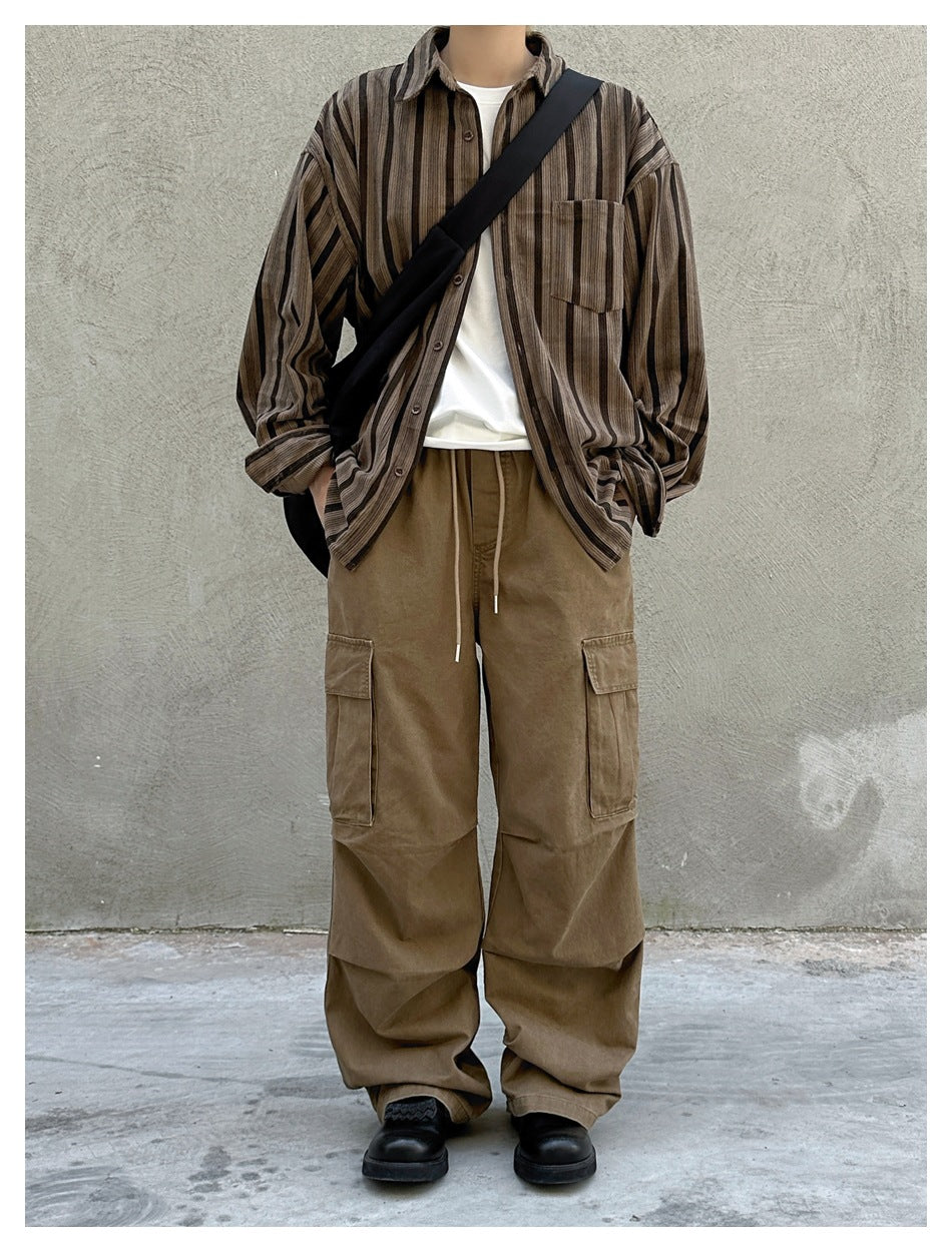 Front view of a model wearing loose brown drawstring cargo pants with large thigh pockets and a striped button-up shirt.