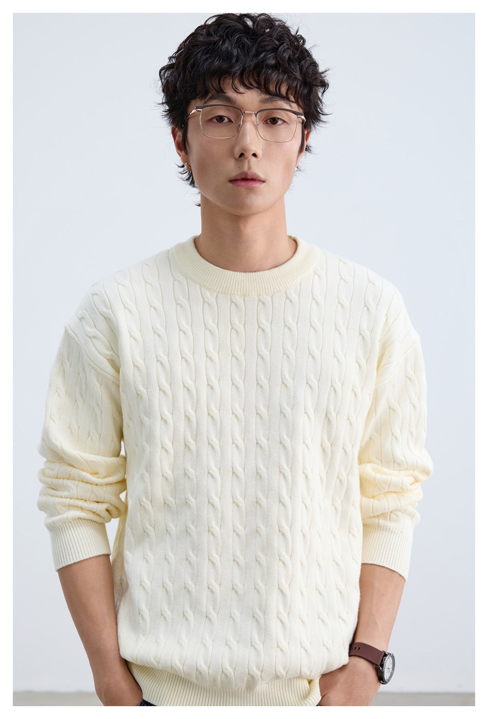 Close view of an ivory cable-knit crewneck sweater worn by a model, showing its braided knit and ribbed collar.