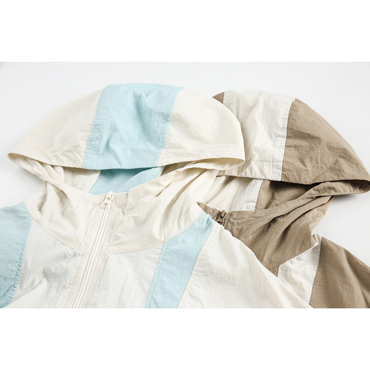 Close-up of two color-block hooded jackets in ivory and pale blue, and taupe and ivory, showing their hoods and front