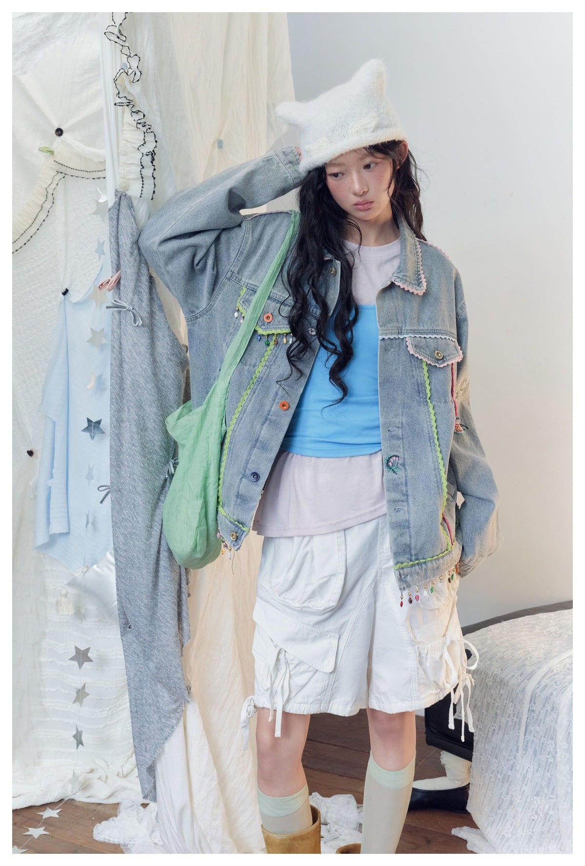Closer view of a model wearing a light-wash denim jacket with colorful trim, floral embroidery, and dangling beads.