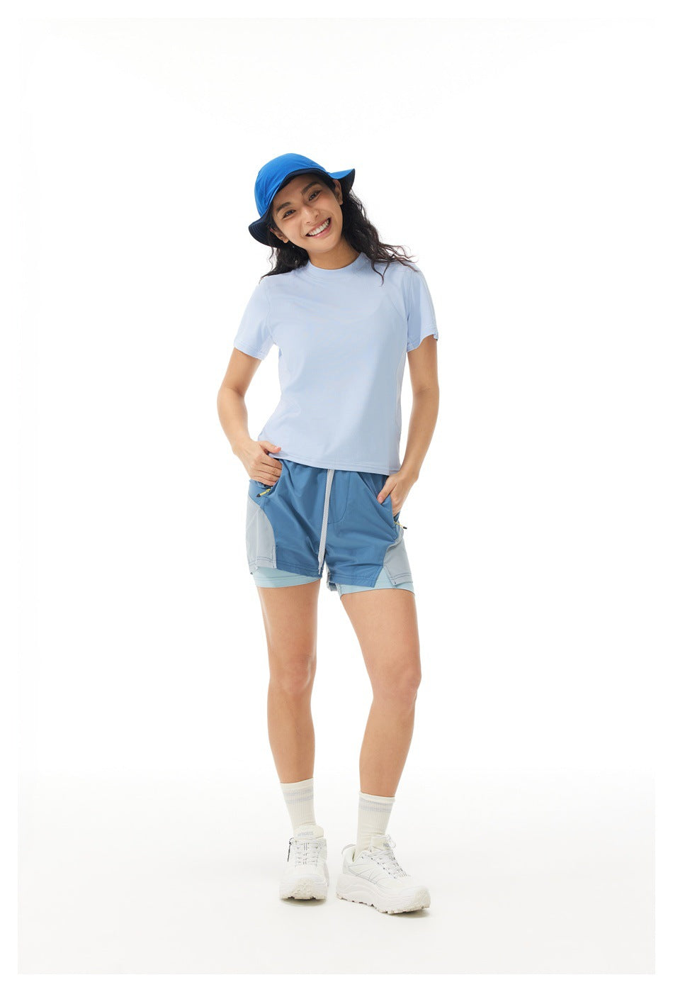 Model wears a pale blue T-shirt and blue layered athletic shorts with a blue cap against a white background.