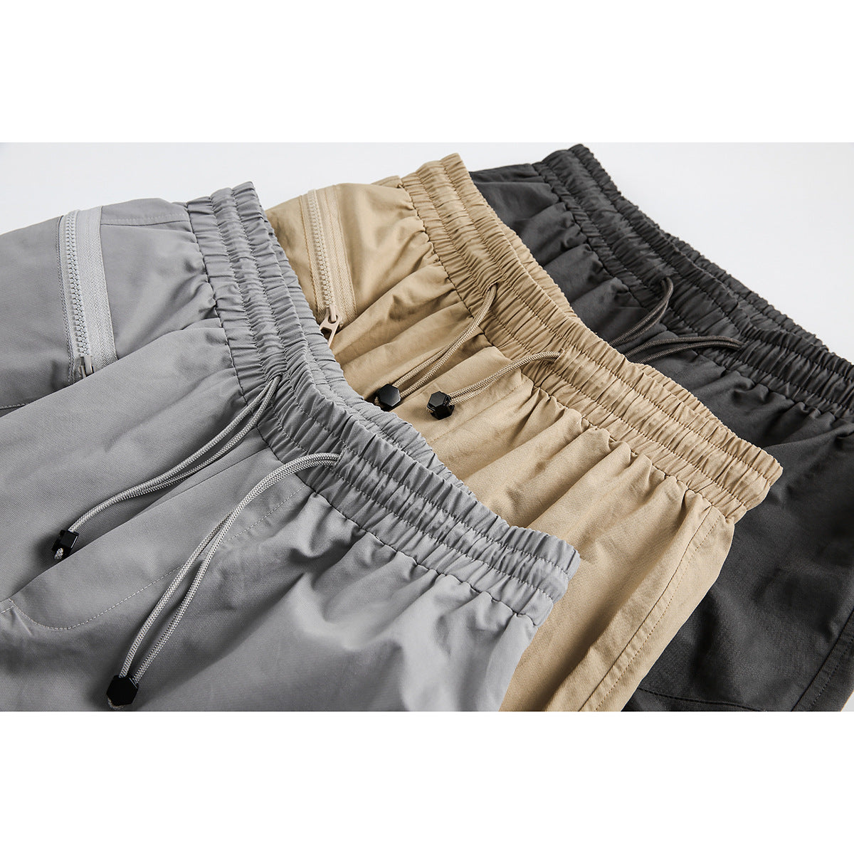 Close-up of gray, tan, and charcoal shorts showing elastic drawstring waists and zip pockets.