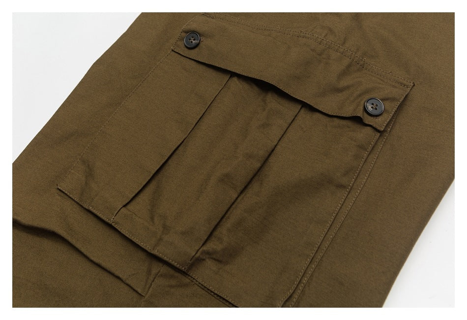 Close-up of a large pleated cargo pocket on brown pants, with a flap secured by two buttons.