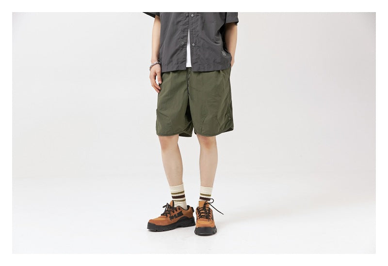 Model wearing olive-green knee-length shorts with a dark short-sleeve shirt, shown from the front.