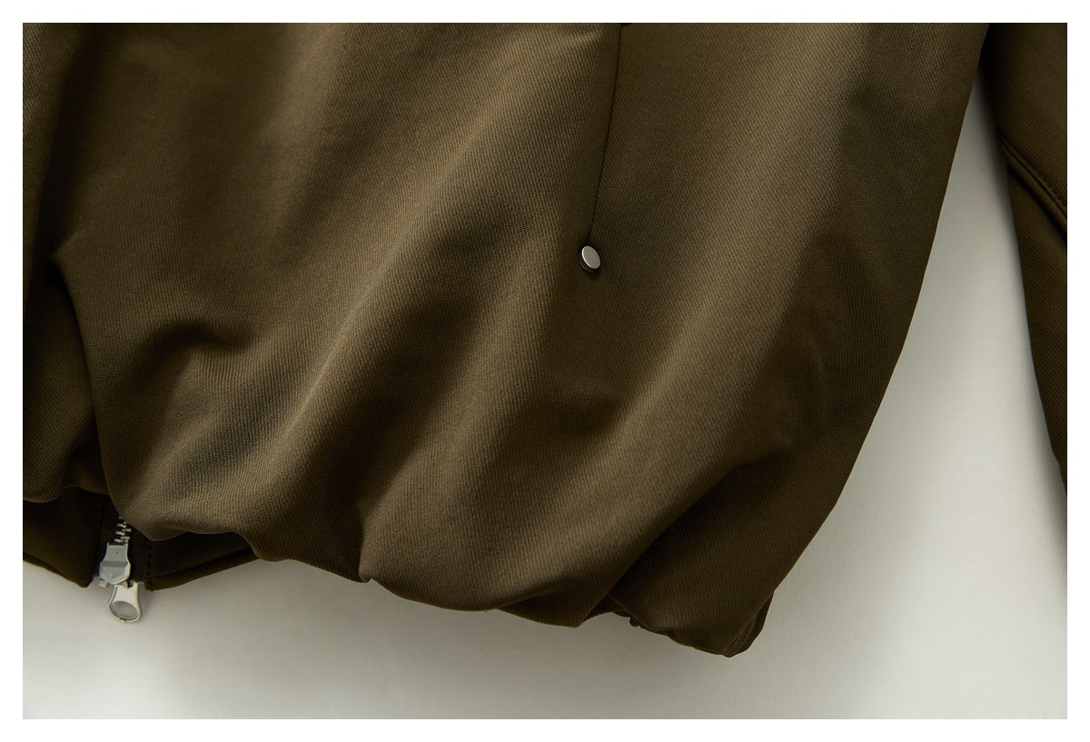 Close-up of an olive-brown garment hem with a metal snap and zipper pull.