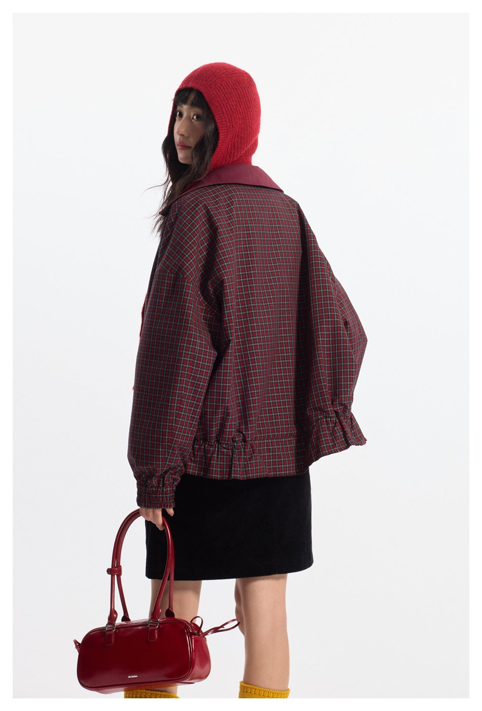 Model wearing a red-and-black plaid jacket with a burgundy collar, shown from the back in a red knit hood.