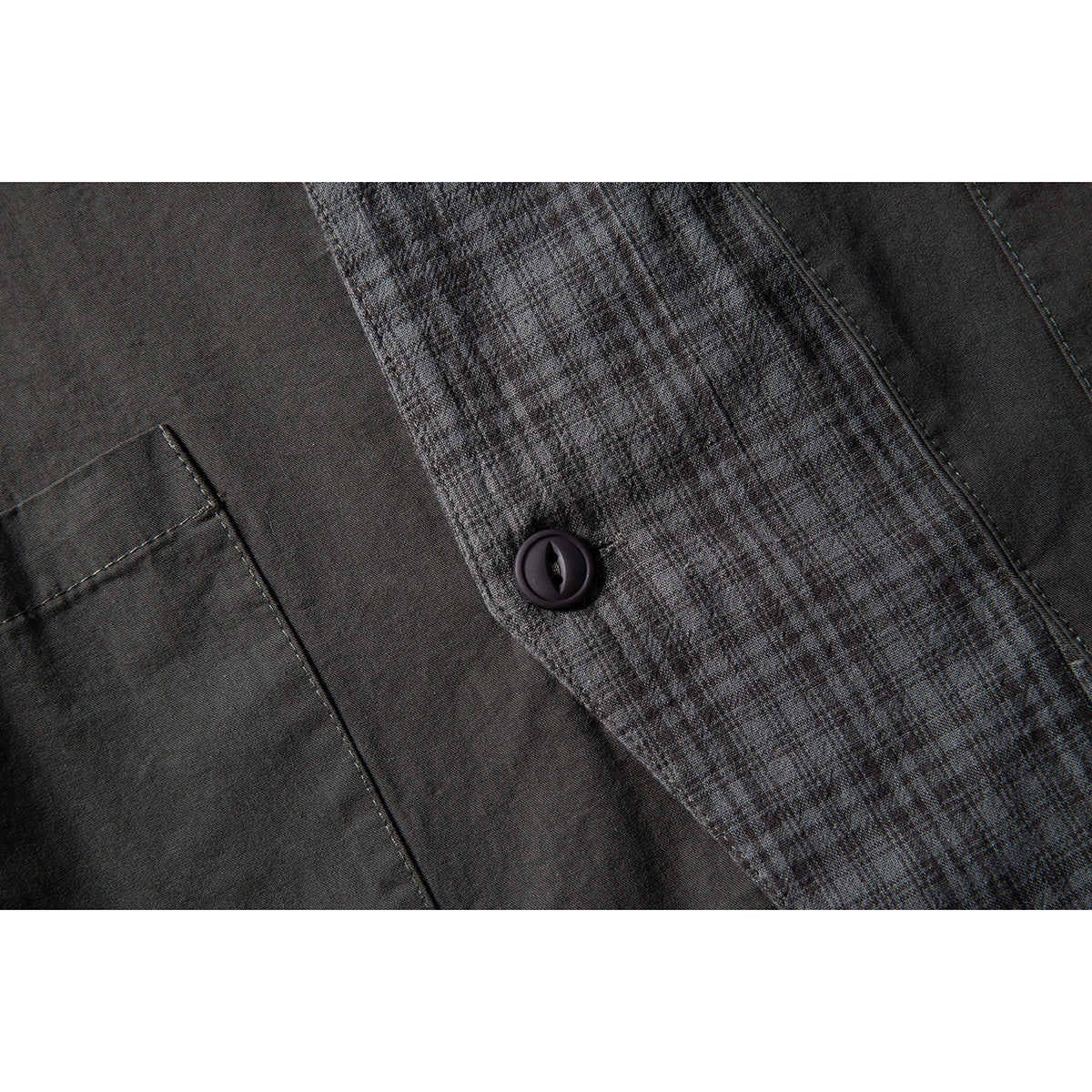 Close-up of a dark button, checked inner placket, and pocket seam on a charcoal garment.