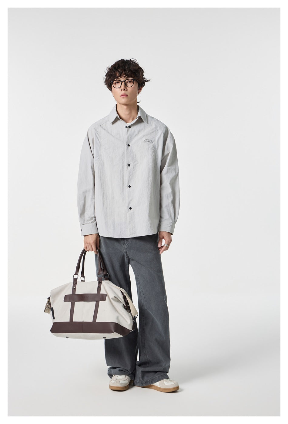 Model wearing a light gray button-up shirt with dark buttons and small chest lettering, paired with gray jeans.