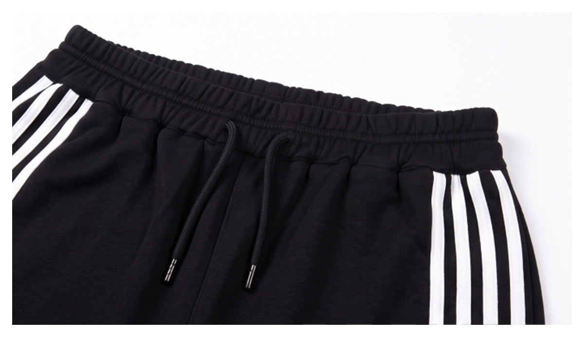 Close-up of black pants showing the elastic waistband, black drawstrings, and white side stripes.