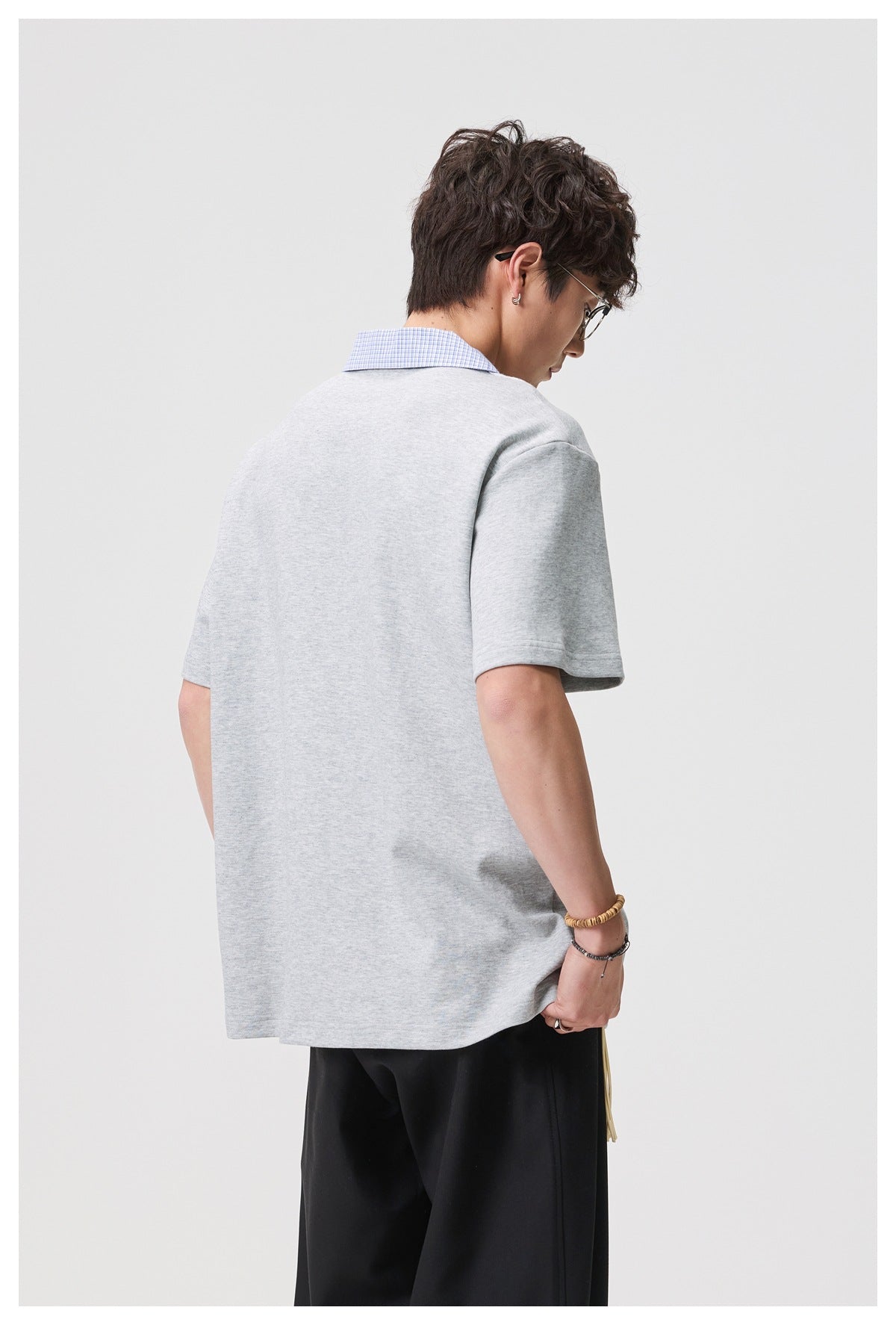 Back view of a man wearing a light gray oversized short-sleeve top with a blue checked collar.