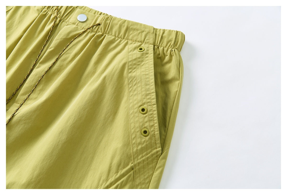 Close-up of yellow-green pants with an elastic waistband and a stitched side panel with snap buttons.