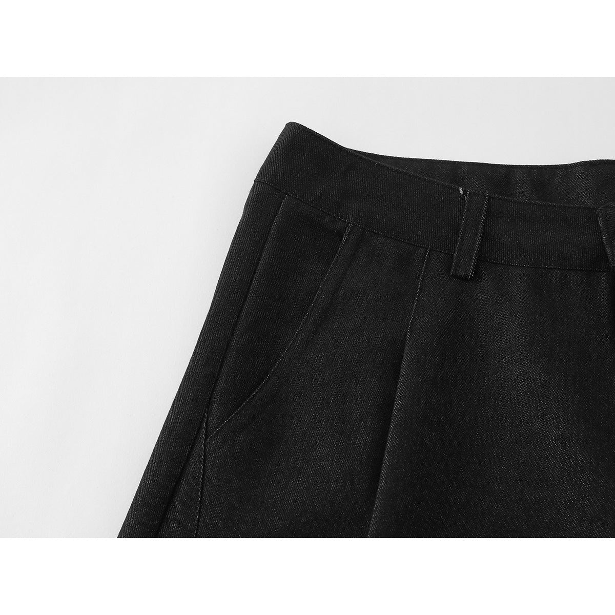 Close-up of black shorts showing a belt loop, waistband, and stitched front pleats.