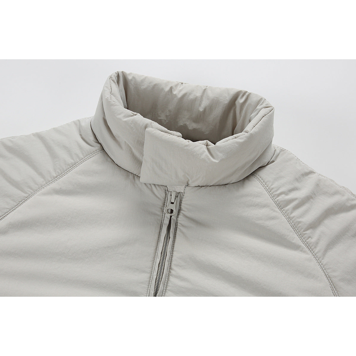 Close-up of a light gray jacket’s high collar, center zipper, and curved shoulder seams.