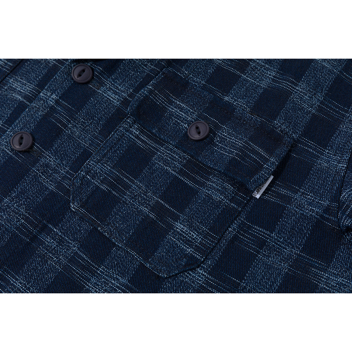 Close-up of a navy plaid shirt chest pocket, dark buttons, and a small sewn label.
