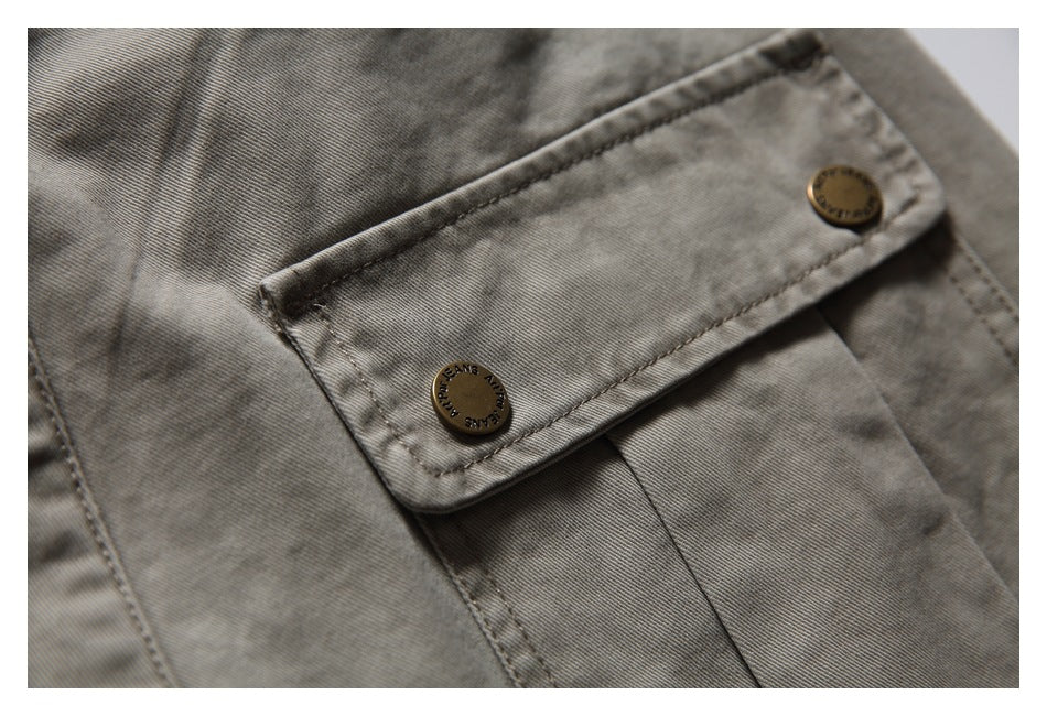 Detailed view of a buttoned pocket flap with metal buttons on taupe-gray trousers.
