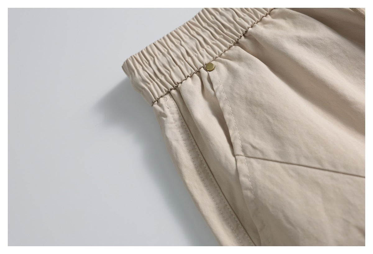 Close-up of beige trousers showing the elastic waistband and a side pocket with a small metal rivet.