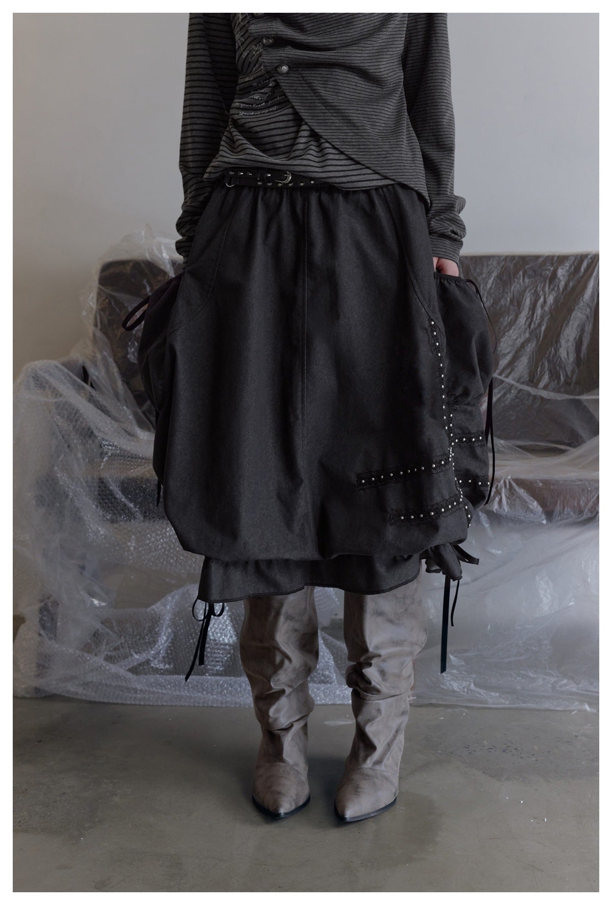 Close front view of a charcoal gathered skirt with studded trim and side ties, worn with a striped top.