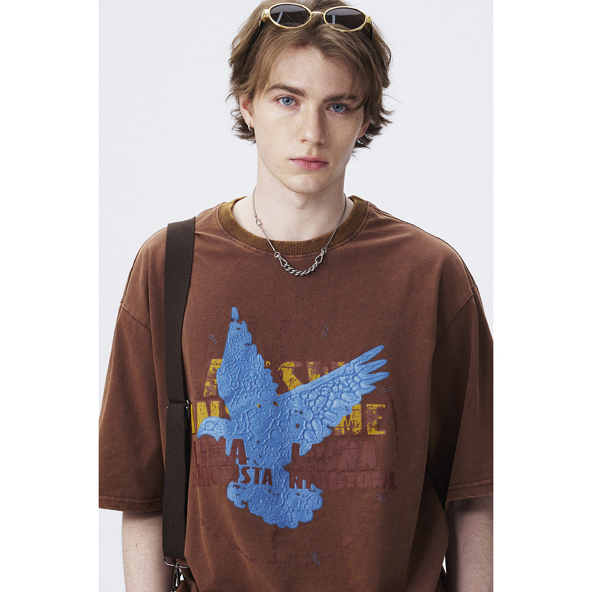 Close-up of a brown T-shirt showing its large textured blue eagle graphic and distressed yellow lettering.