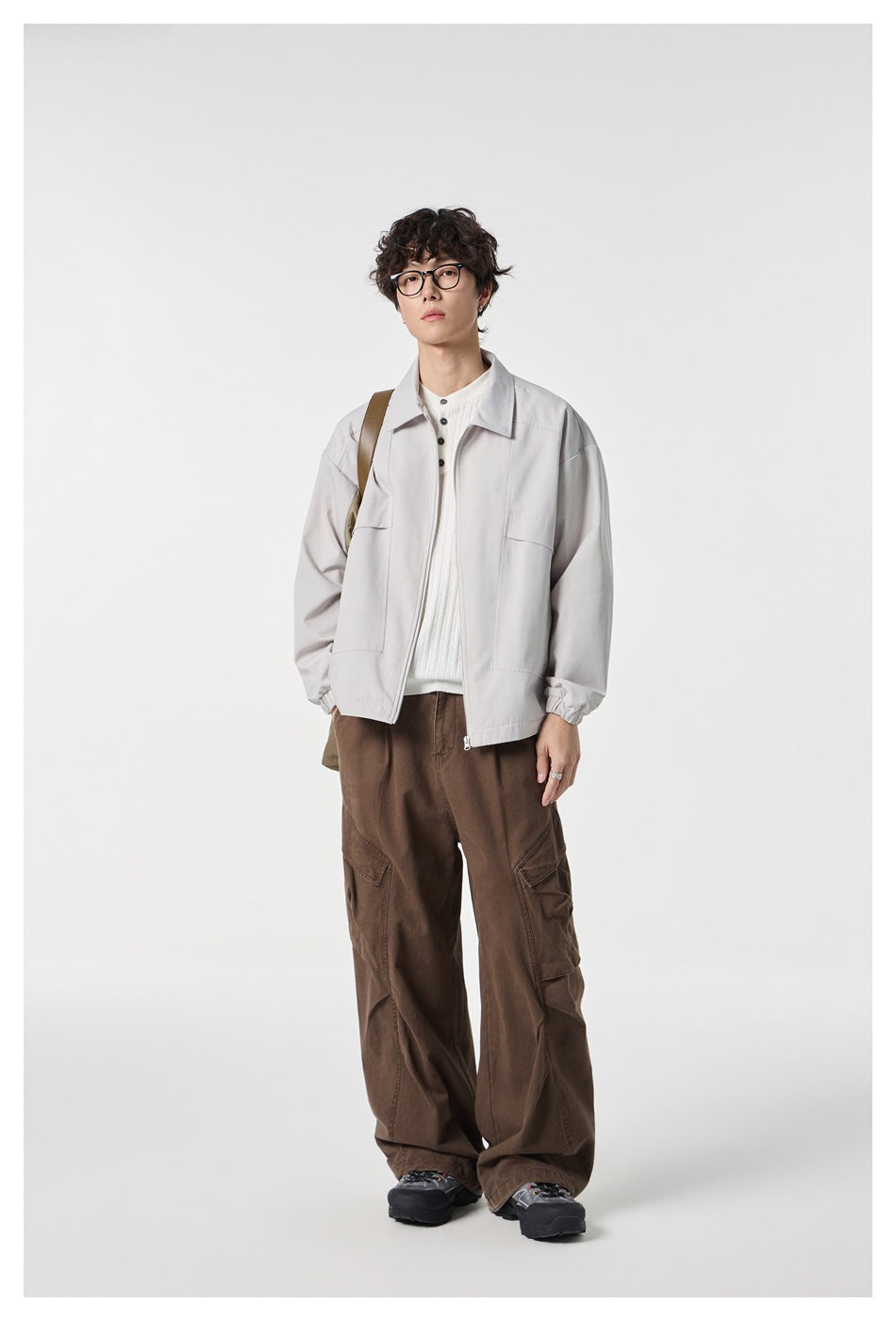 Model wearing a light gray zip-front jacket with a pointed collar and large front pockets, paired with brown cargo pants.