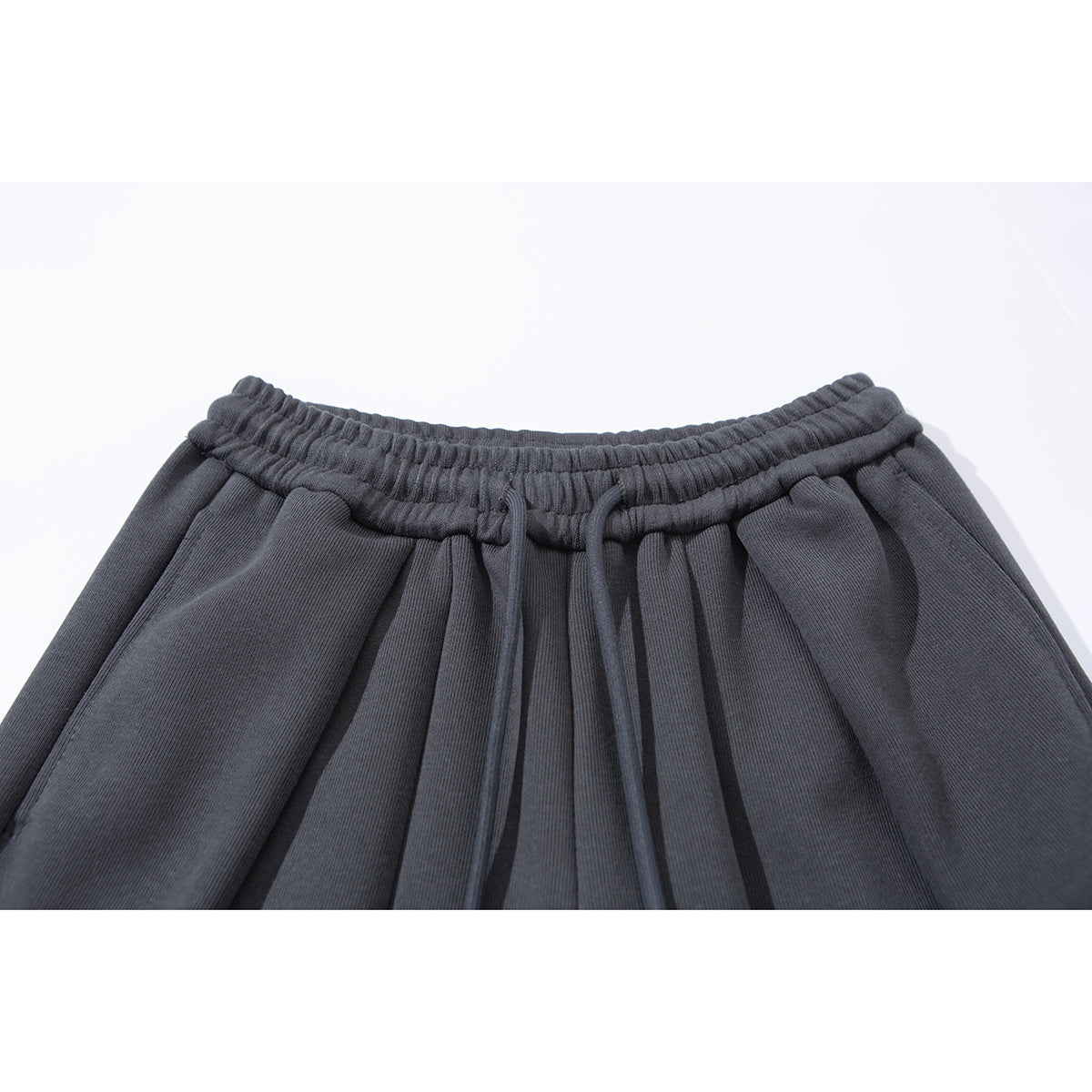 Close-up of charcoal wide-leg pants showing the elastic waistband, front drawstrings and pleats.