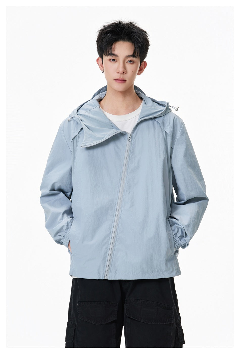 Front view of a model wearing a pale blue-gray hooded jacket with an asymmetrical zipper and black cargo pants.