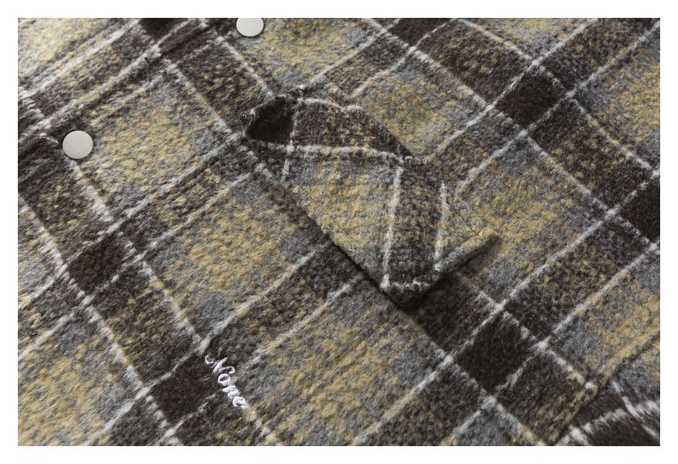 Close-up of a plaid jacket's flap pocket, silver snaps, and small white embroidery.