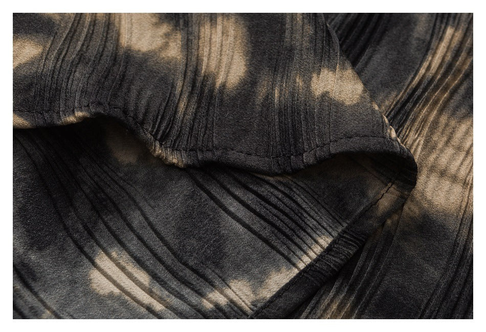 Close-up of a stitched folded edge on dark fabric with beige abstract print and narrow pleats.