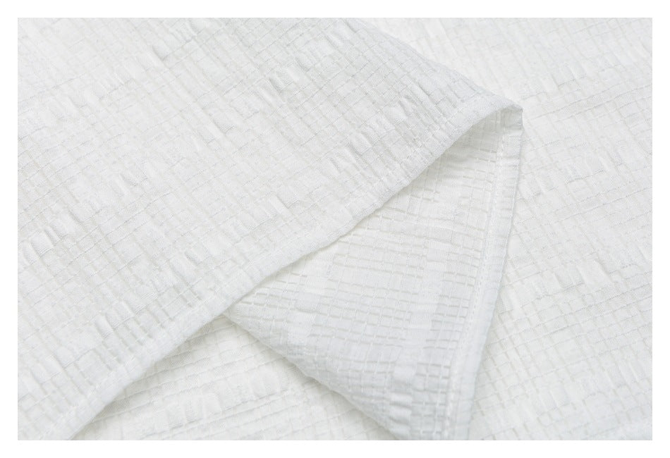 Close-up of overlapping white shirt fabric panels with a folded edge and geometric texture.