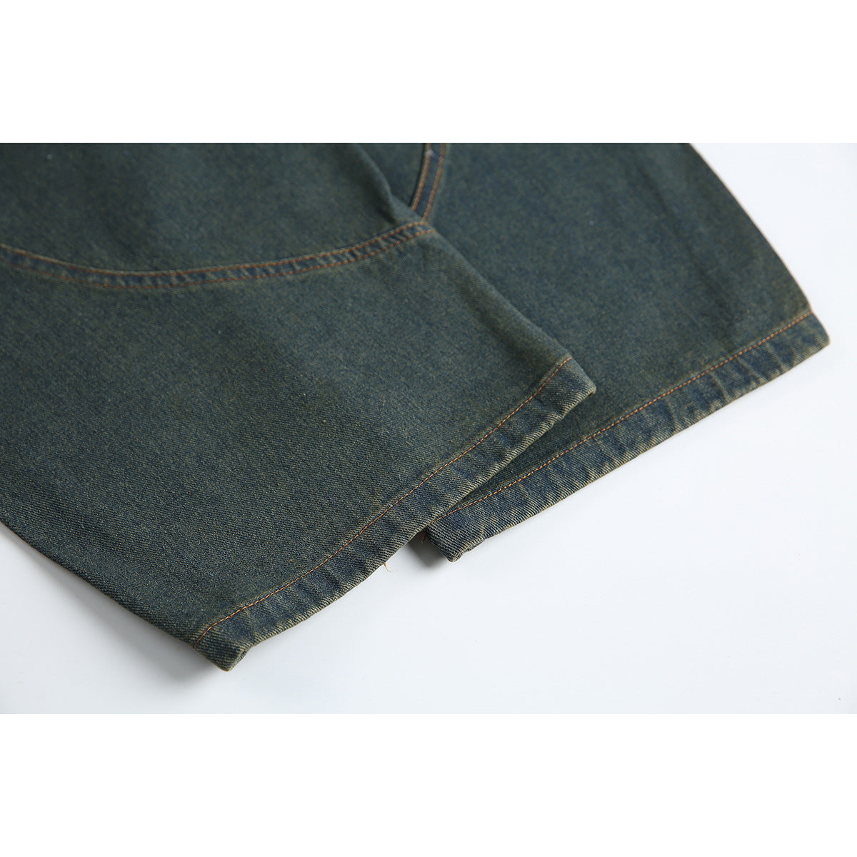 Close-up of dark indigo jeans showing a leg hem and orange contrast stitching.
