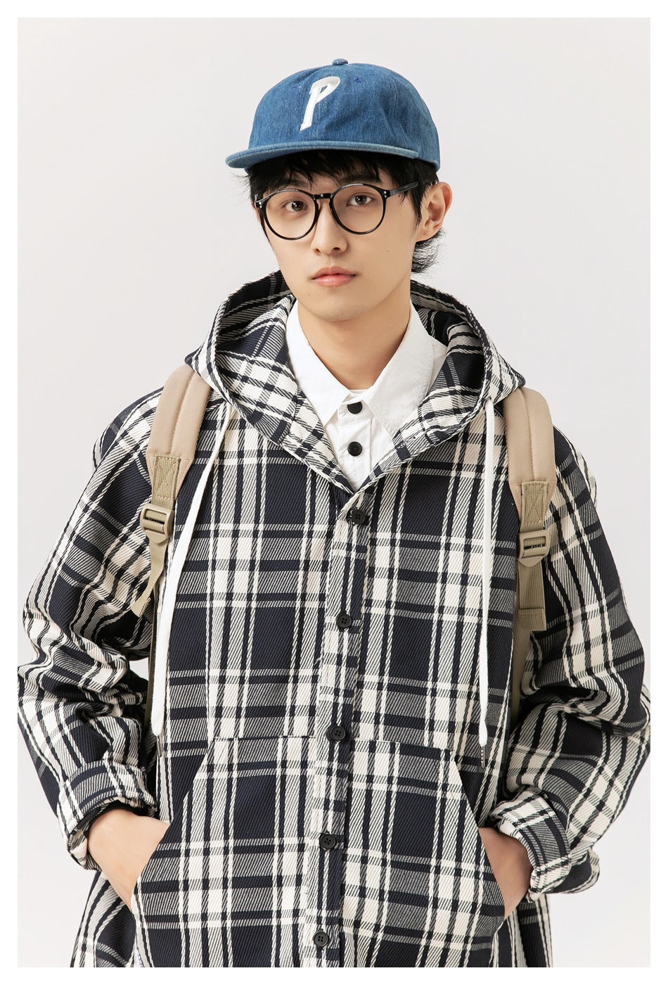 Front close-up of a model wearing a black-and-white plaid hooded button coat with front pockets.