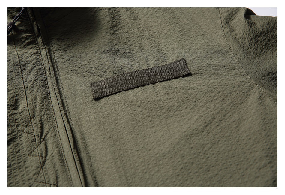Close-up of an olive jacket's textured fabric and a dark horizontal fabric tab.