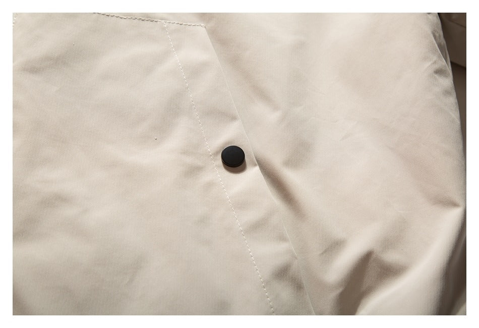 Close-up of a black snap fastener on a beige garment panel with visible stitching.