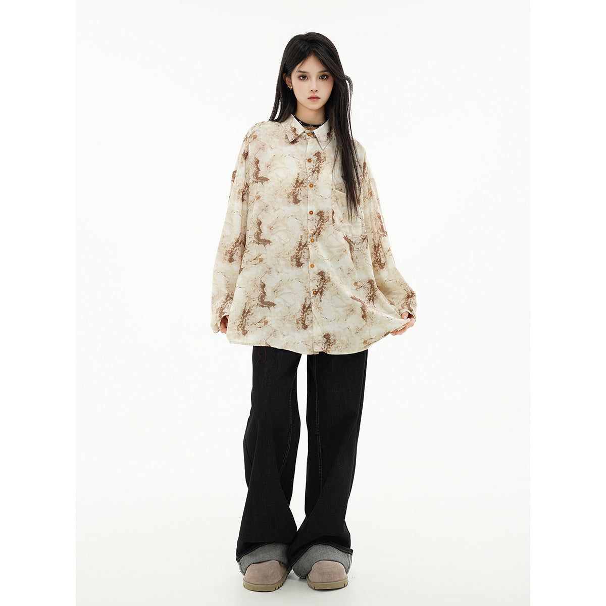 Model wearing an oversized cream and brown abstract-print button-up shirt with black wide-leg jeans and taupe shoes.