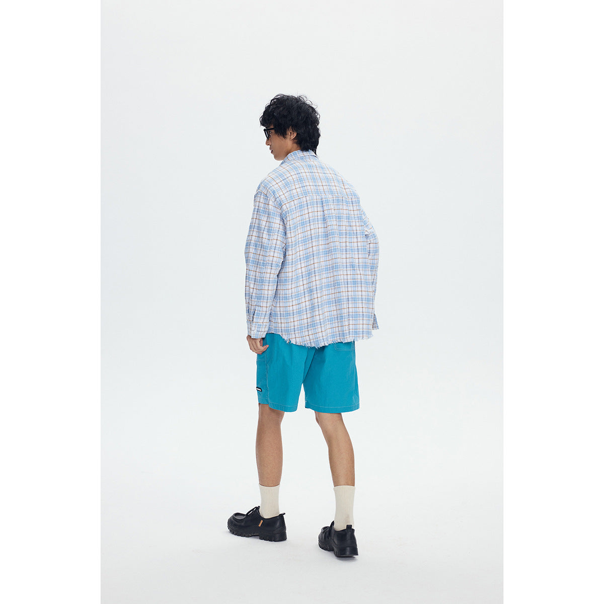 Back view of a model wearing a blue-and-tan plaid shirt with a frayed hem and turquoise shorts.