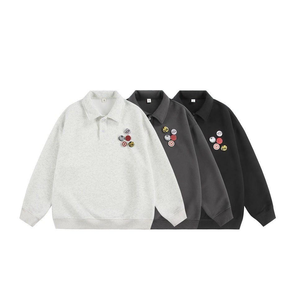 Three polo-collar pullovers in light gray, dark charcoal and black, each with a cluster of round badges on the chest