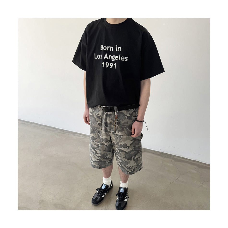 Person wearing loose gray camouflage shorts with a black graphic T-shirt and black sneakers.