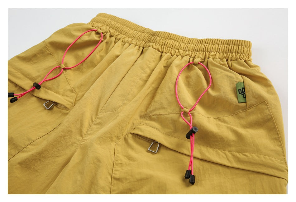 Mustard shorts laid flat, with an elastic waist, large front pockets, and bright pink adjustable drawcords.