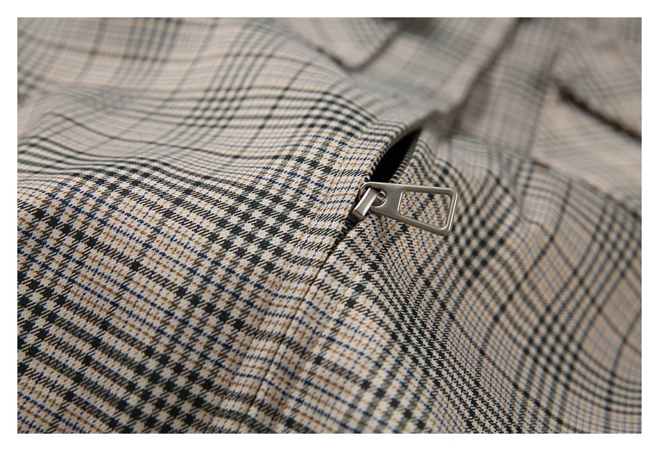 Close-up of a metal zipper pull on a beige, black, and blue plaid garment.