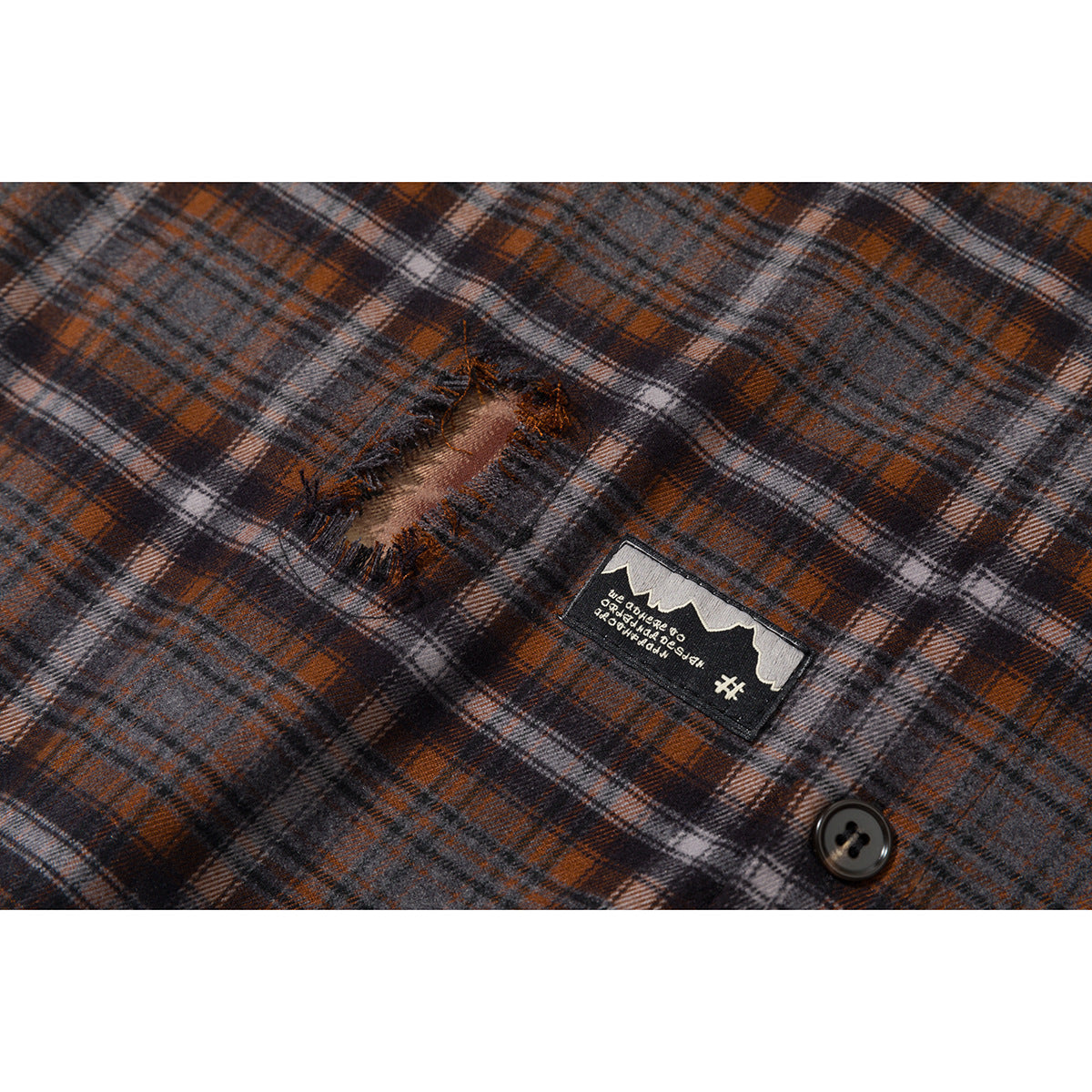 Close-up of gray, rust, and black plaid fabric with a distressed hole, a sewn patch, and a dark button.